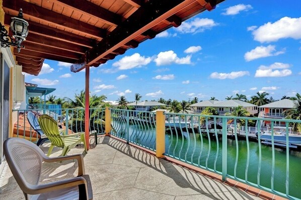 A balcony with a view of a marina, a covered area with chairs, and a railing.