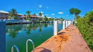 A marina with boats docked, a paved walkway, and residential buildings with balconies. - P21  - Charming 3 bedroom 3.5 bath duplex with dockage and Cabana Club. (Key Colony Beach)