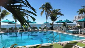 A pool area with lounge chairs and umbrellas, surrounded by palm trees and a view of the ocean. - P21  - Charming 3 bedroom 3.5 bath duplex with dockage and Cabana Club. (Key Colony Beach)