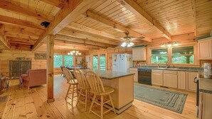 A wooden cabin interior with a kitchen, dining area, and a bar. - Log Cabin right next to entrance of the Great Smokey Mountains National Park! (Waynesville)