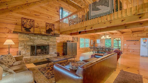 A spacious log cabin interior with a stone fireplace, leather sofas, and a balcony with a railing. - Log Cabin right next to entrance of the Great Smokey Mountains National Park! (Waynesville)