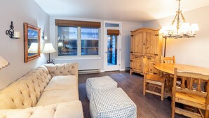 A living room with a sofa, ottomans, a dining table with chairs, a chandelier, and a wooden cabinet. - Cozy Condo steps to Coonskin lift (Telluride)