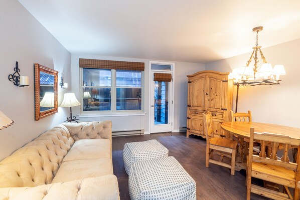 A living room with a sofa, ottomans, a dining table with chairs, a chandelier, and a wooden cabinet. - Cozy Condo steps to Coonskin lift (Telluride)