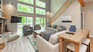 Ein geräumiges Wohnzimmer mit hoher Decke, großen Fenstern, einer Holztreppe und einem Kamin.