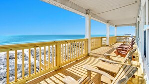 A covered deck with wooden furniture and a view of the beach.