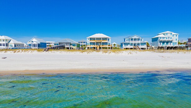 Beachfront houses with balconies and a sandy beach in the foreground.