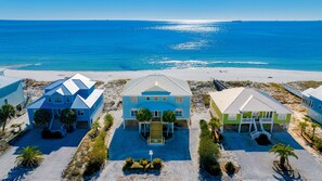 Um imóvel à beira-mar com três casas, uma praia de areia e o oceano.