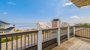 Een houten terras met een leuning, met uitzicht op een strand en huizen.