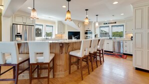 A modern kitchen with a central island, bar stools, stainless steel appliances, and pendant lighting. - Huge Oceanfront Home with Full Golf Membership (Georgetown)