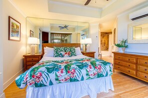A bedroom with a large bed, a wooden dresser, a mirror, and a ceiling fan.