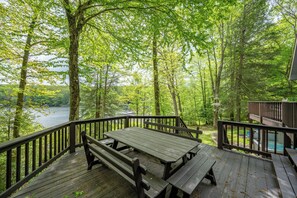 A wooden deck with picnic tables overlooking a lake surrounded by trees. - Stylish Lake Retreat w/ Hot Tub, Dock & Fire Pit (Oakland)