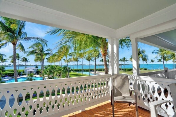A balcony with a view of a pool and palm trees, overlooking a beach and ocean.