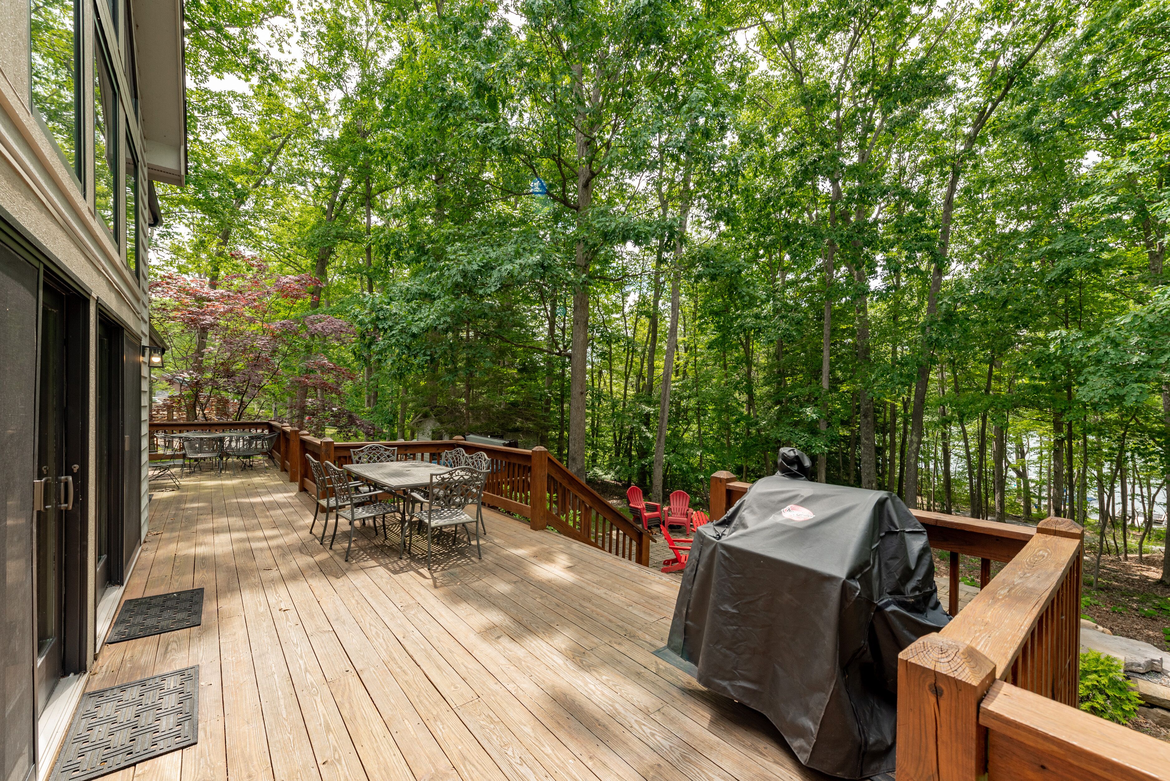 A wooden deck with outdoor furniture, a covered grill, and a view of a forested area.