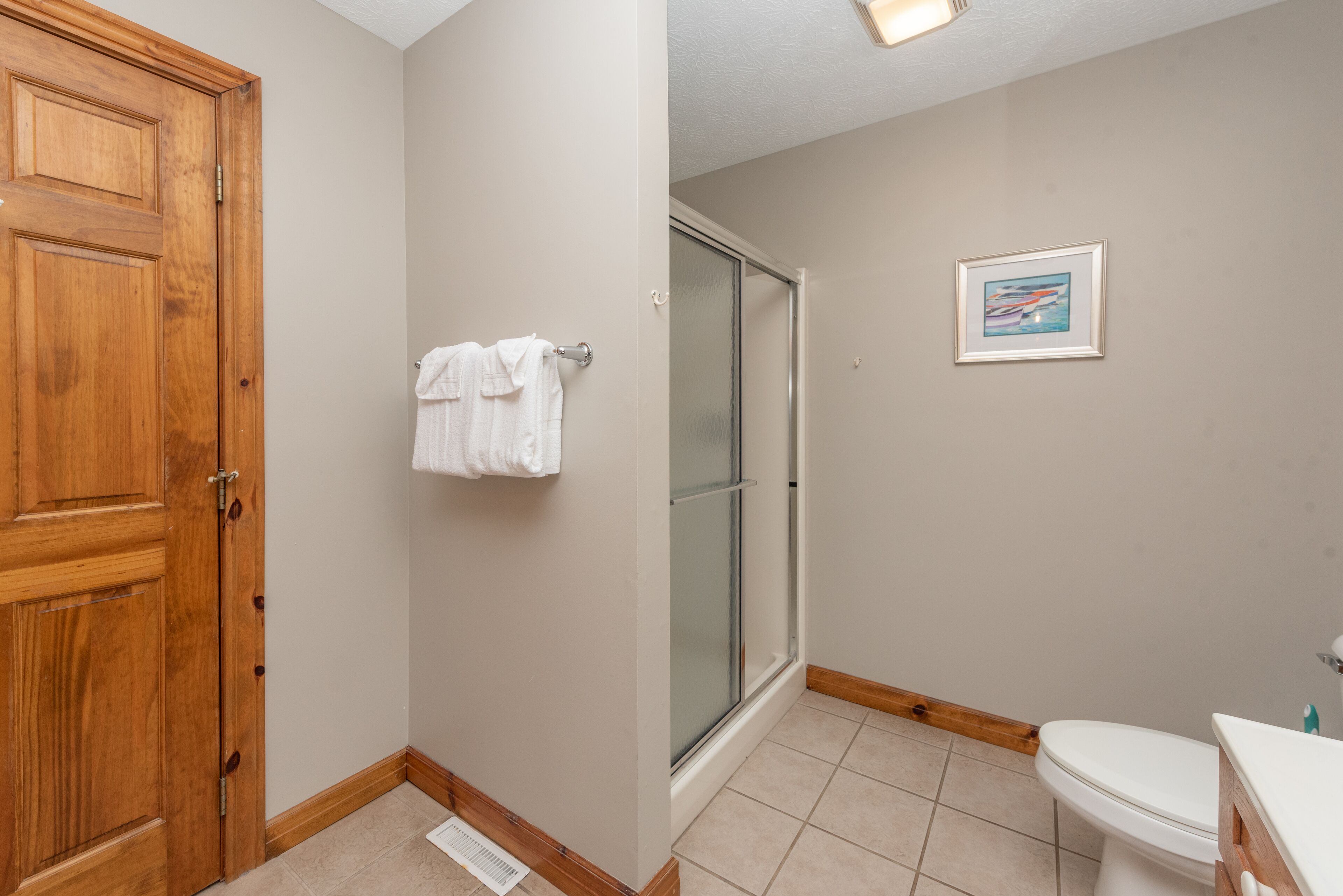 Un baño con puerta de madera, mampara de cristal, inodoro y un cuadro en la pared.