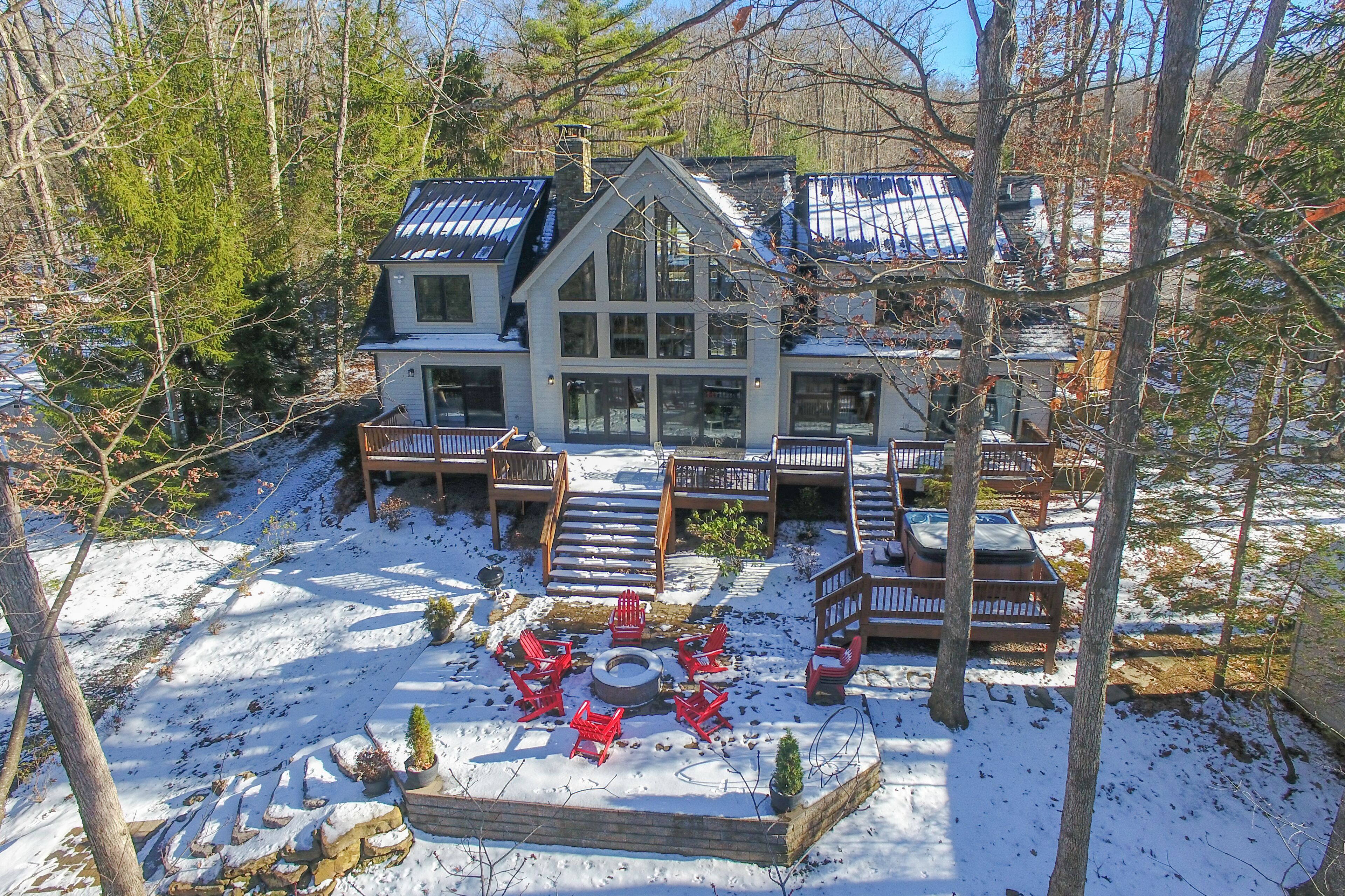 A large house with a deck, a fire pit, and red chairs.