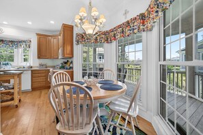 A kitchen with wooden cabinets, a dining table with chairs, a chandelier, and large windows with a view.