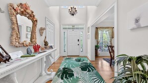 A hallway with a white console table, a mirror with a shell frame, a tropical-themed rug, and a chandelier. - Inviting Beach Retreat with wonderful Lake Views to Relax and Enjoy (Georgetown)