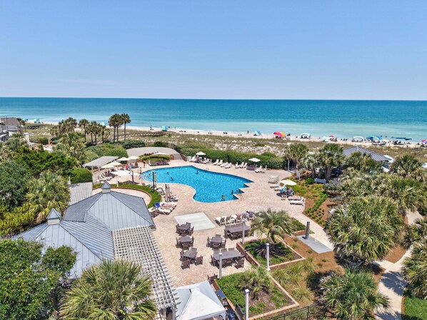 A resort with a swimming pool, beach, and palm trees.
