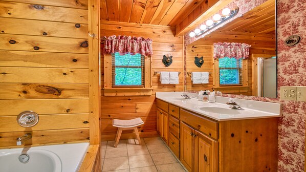 A wooden cabin bathroom with a bathtub, two sinks, a vanity, and a mirror.