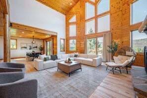 A spacious living area with a large sofa, a coffee table, and a wicker chair. There is a dining area with a table and chairs visible in the background. - Elegant Escape Steps from Lake & Fun (McHenry)