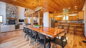 Een ruime keuken met een houten plafond, een stenen openhaard en een eethoek met een lange tafel en stoelen.