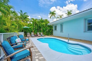 Une piscine entourée de palmiers et d’un bâtiment bleu clair, avec des chaises longues et des parasols à proximité.