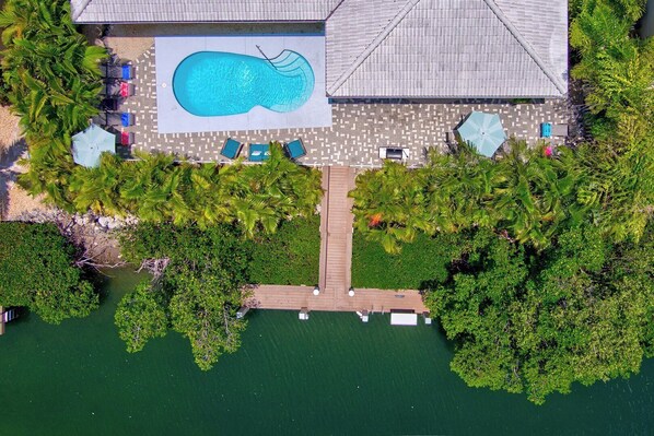 Vue aérienne d’un complexe hôtelier doté d’une piscine, de chaises longues et d’une terrasse en bois.