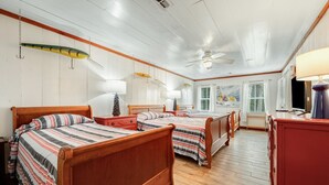 Une chambre avec deux lits en bois, un ventilateur de plafond et une fenêtre avec des stores.