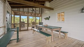 Un espace extérieur abrité, doté d’une terrasse en bois, d’une table avec des bancs et d’un ventilateur de plafond.