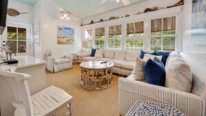 A spacious living room with a large white sofa, a round coffee table, and a ceiling fan. - Spectacular Oceanfront Living with an Inviting Kitchen Perfect for Entertaining Kitchens Beach House (Georgetown)