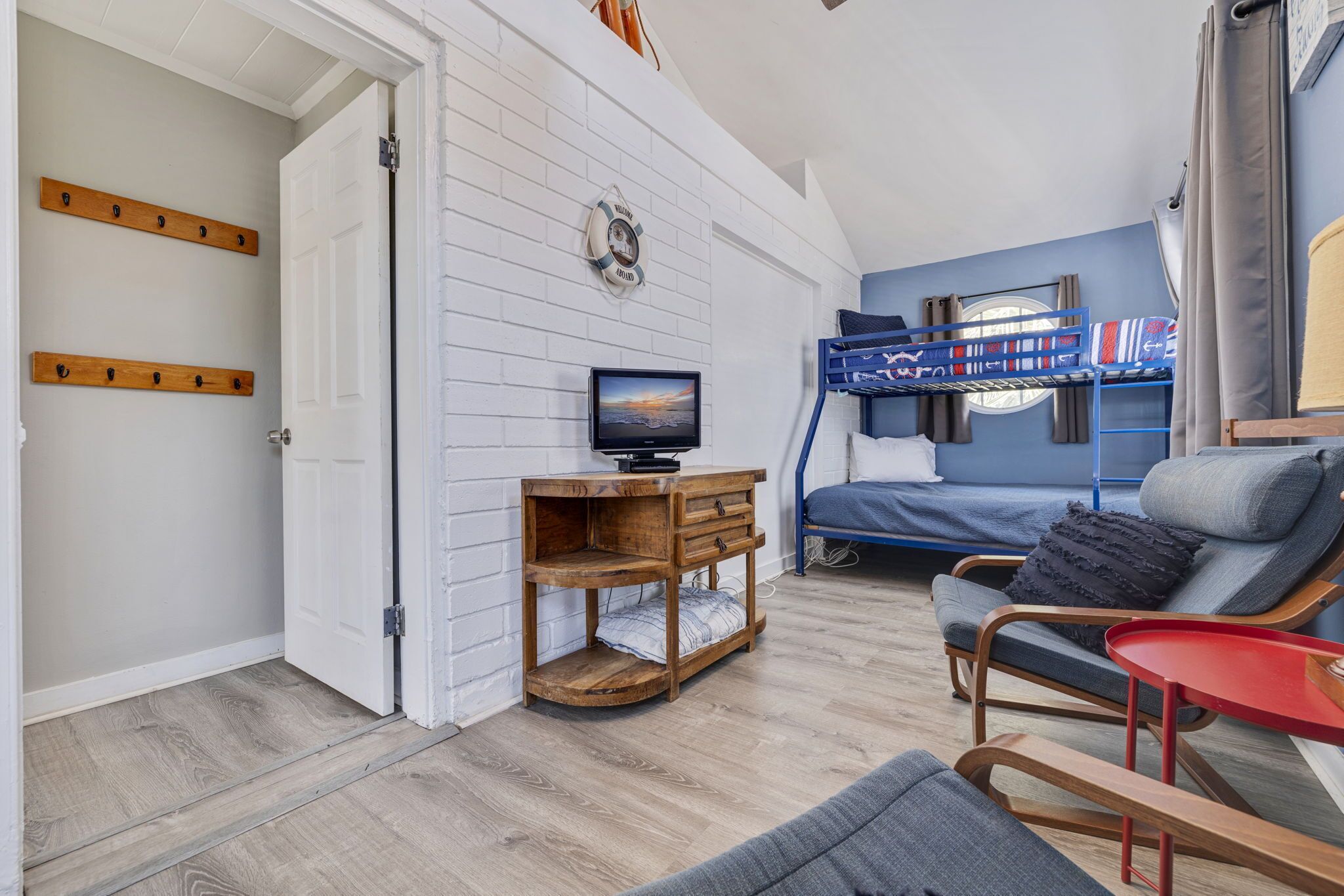 Ein gemütliches Zimmer mit einem Etagenbett, einem HolztV-Schrank, einem roten Beistelltisch und einem grauen Sofa.