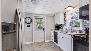 Una cocina moderna con armarios blancos, un refrigerador de acero inoxidable, un horno empotrado y una ventana con vista a follaje.