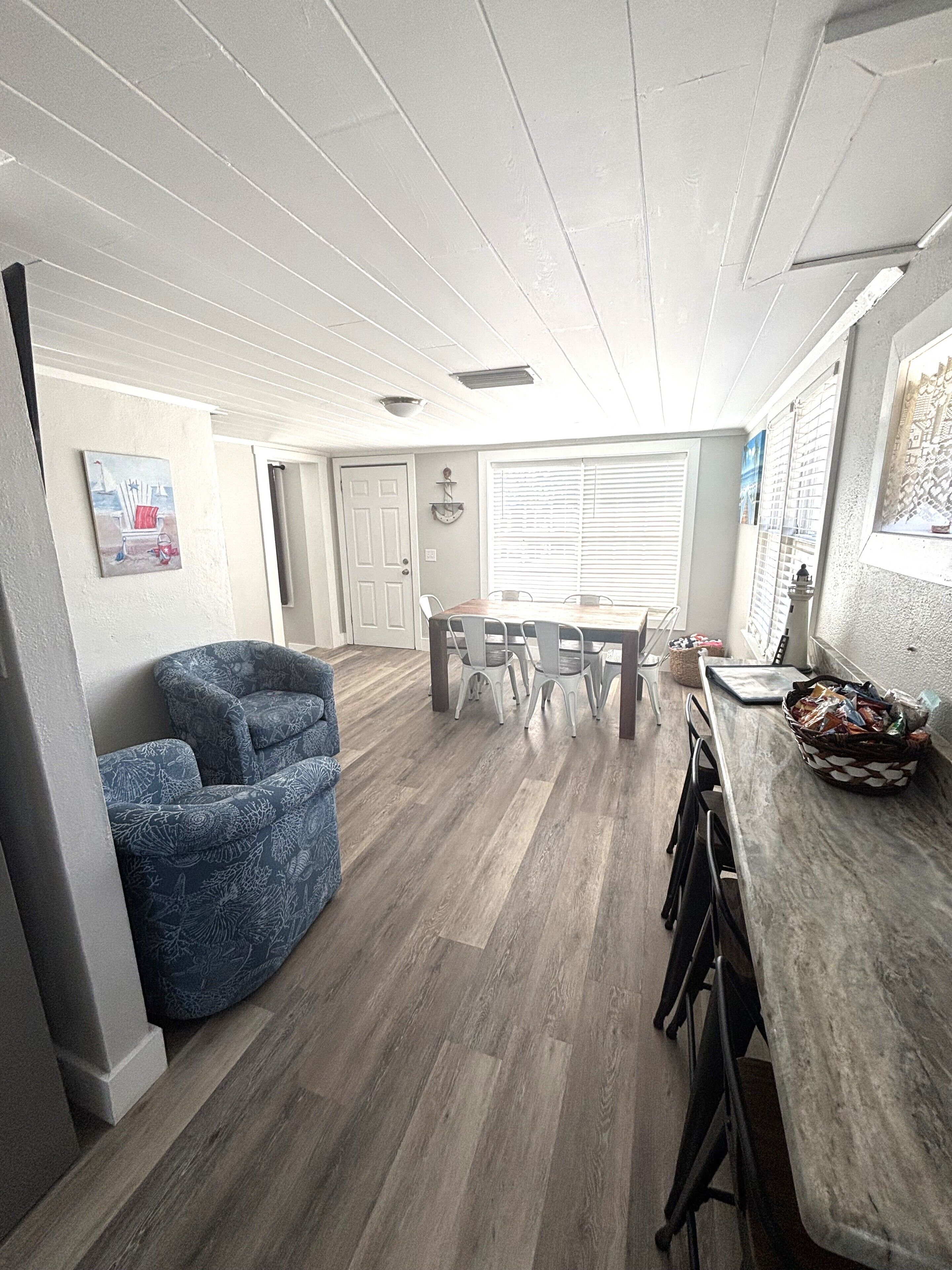 A spacious kitchen with a dining area, wooden flooring, and a blue armchair.