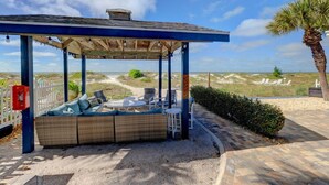 Un espacio al aire libre cubierto con un sofá y sillas de mimbre, una mesita y vistas a la playa y las dunas.