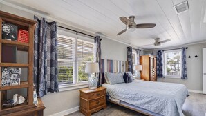 Un dormitorio con cama, mesita de noche de madera, ventilador de techo y estantería.