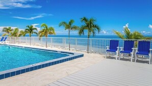 Une piscine avec vue sur l’océan, entourée de palmiers et de chaises bleues.