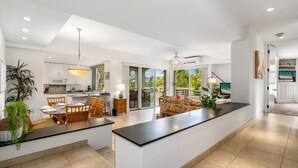A modern kitchen with a central island, dining area with chairs, and a large window providing a view of the outdoors. - Wailea Condo Near Keawakapu Beach with Pool & Tropical Setting (Wailea)