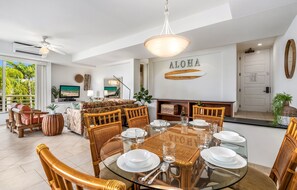 Un vaste espace de vie comprenant un coin repas avec une table pour quatre personnes, entourée de chaises en osier.