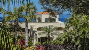 A building with arched windows and a red-tiled roof, surrounded by lush greenery and palm trees. - Wailea Condo Near Keawakapu Beach with Pool & Tropical Setting (Wailea)