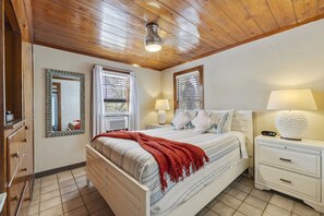 A bedroom with a wooden ceiling, a bed with striped bedding, a red throw blanket, a bedside lamp, and a nightstand with a lamp.