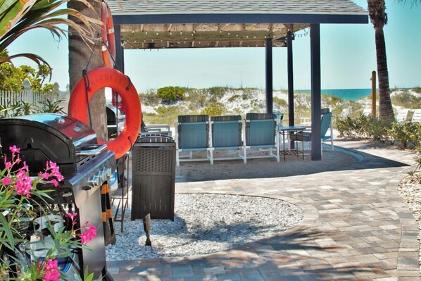 A covered outdoor seating area with a grill, lounge chairs, and a lifebuoy.