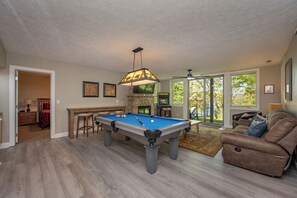 A pool table in a room with a ceiling fan, a fireplace, and a view of the outdoors. - Dog Friendly Deep Creek Retreat w/ Hot Tub (Oakland)