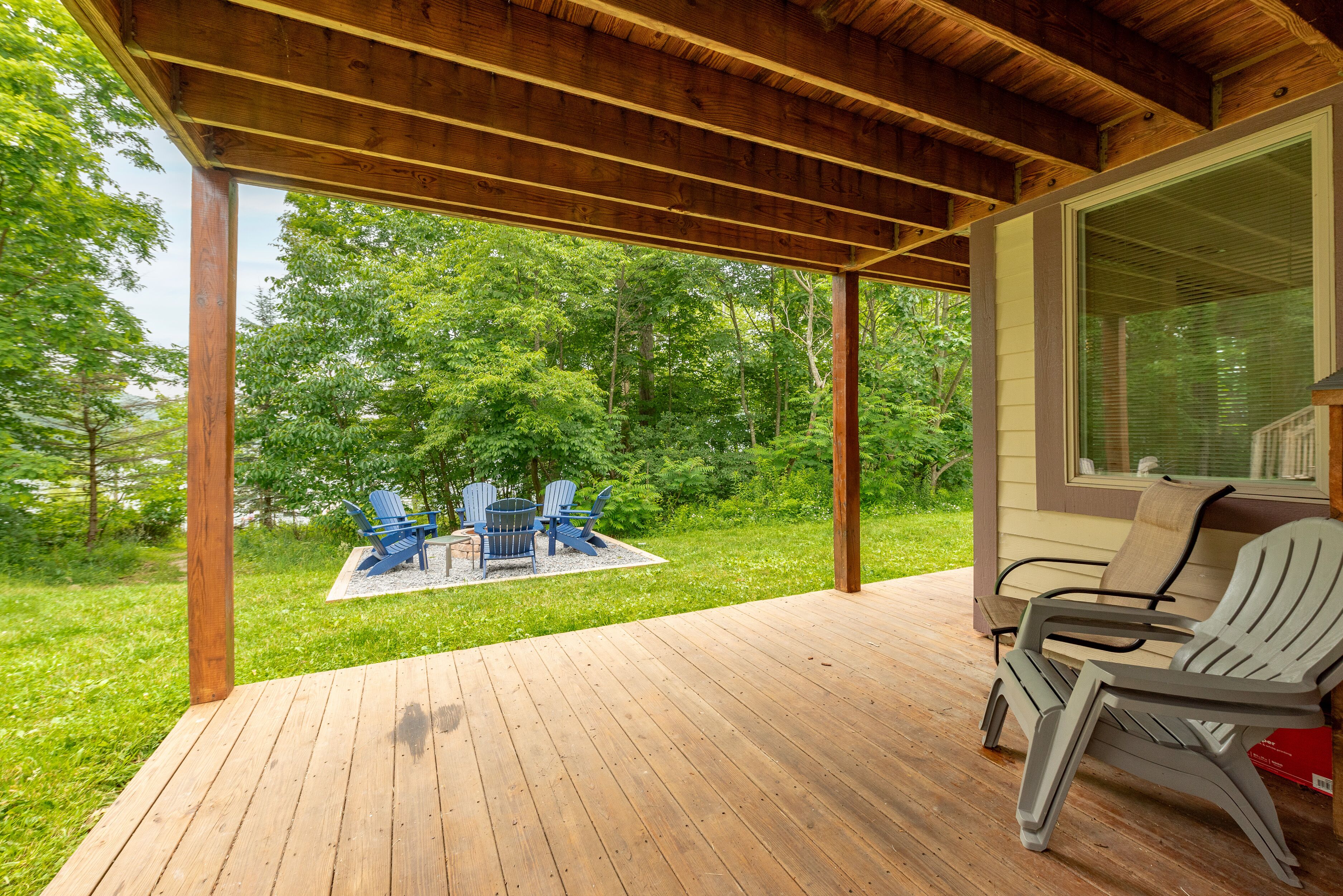 Een houten terras met Adirondack-stoelen en een vuurkuil, met uitzicht op een weelderig groon landschap.