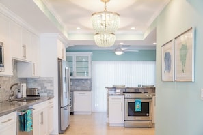 A modern kitchen with white cabinetry, stainless steel appliances, a chandelier, and a ceiling fan. - P03 - Charming 4 bedroom home with pool and dock. (Marathon)