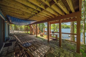 Um terraço coberto ao ar livre com guarda-corpo de madeira, uma mesa e cadeiras.