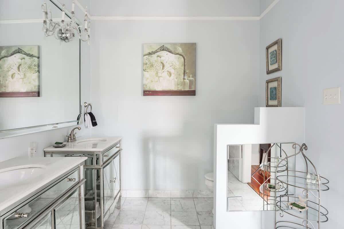 A modern bathroom with a glass vanity, a chandelier, and artwork on the walls.