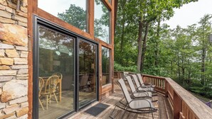 Eine Holzterrasse mit Sitzgelegenheiten im Freien, eine Steinmauer und große Glasüren, die zu einem Innenraum führen.