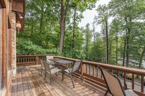 A wooden deck with a table and chairs, surrounded by trees and overlooking a body of water. - Rustic Chalet w/ Fireplaces & Jetted Tub (McHenry)