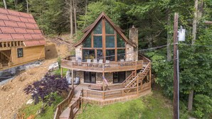Eine Hütte mit einer zweistöckigen Terrasse, großen Fenstern und einem Steinkamin.