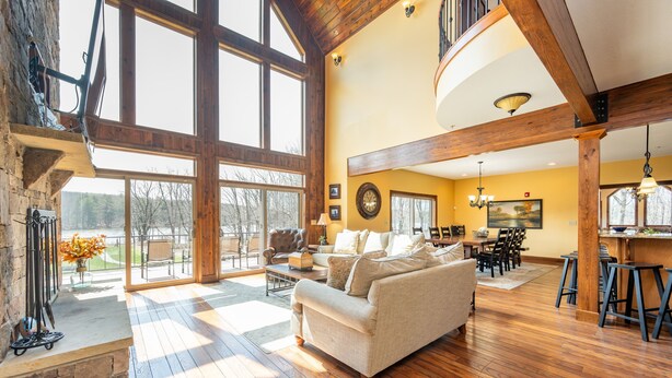A spacious living room with a large window, wooden flooring, and a cozy fireplace. - Luxury Lake Escape w/ Indoor Pool & Hot Tubs (Swanton)
